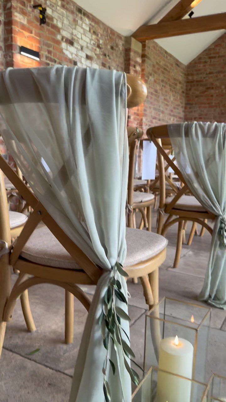 Sage green fabric and olive leaves decorating light wood cross-back wedding chairs.