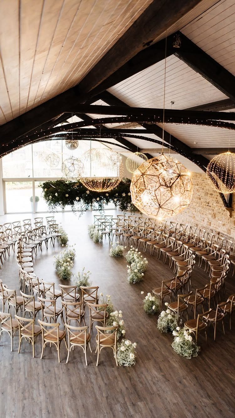 Modern barn interior with vaulted ceilings, geometric lighting, and curved wedding chair seating.