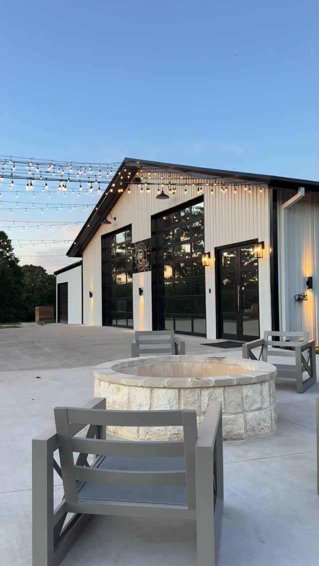 Modern white barn with black trim and a stone fire pit on a patio.