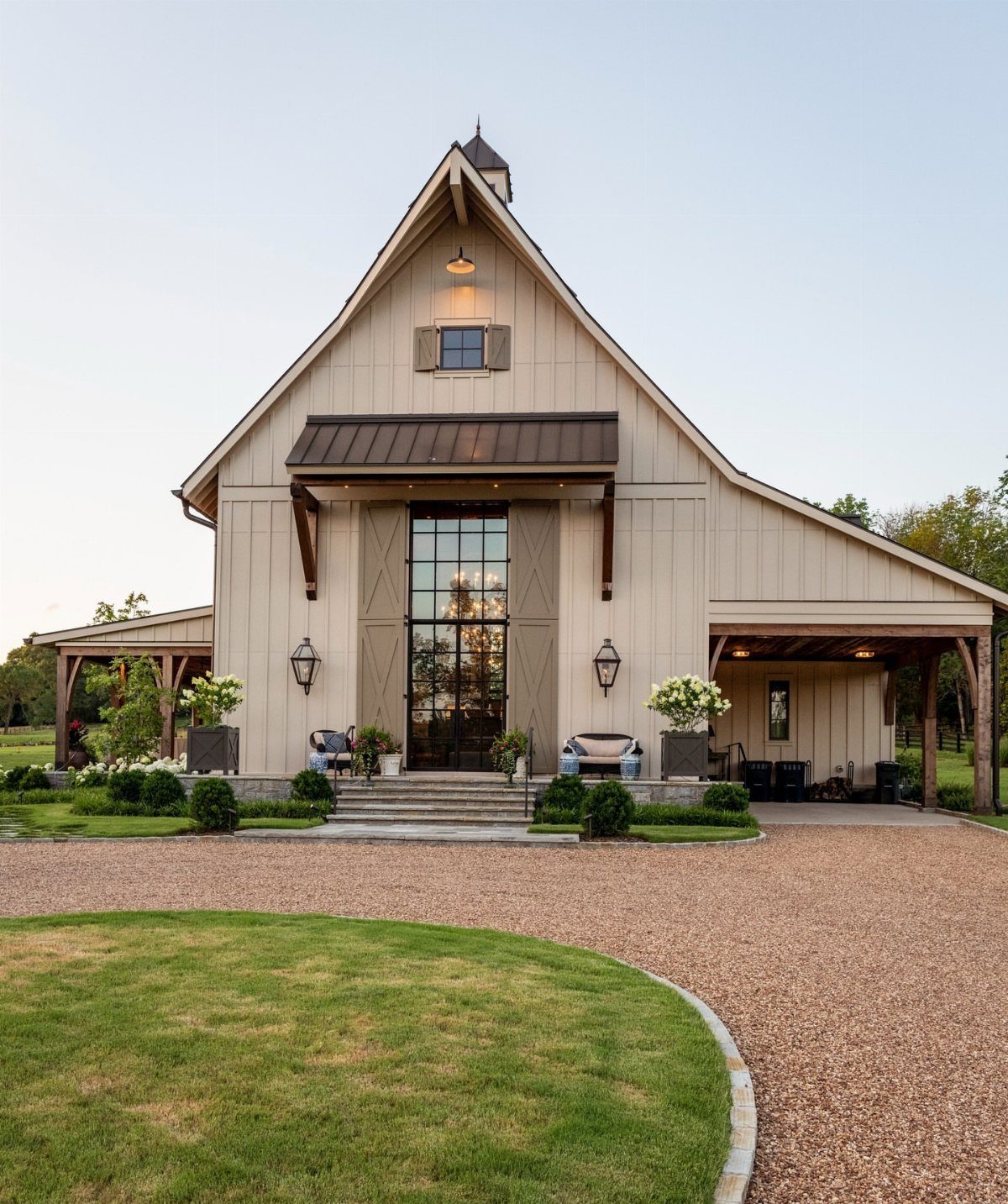 Modern beige barn wedding venue with a gravel driveway and manicured green lawn.