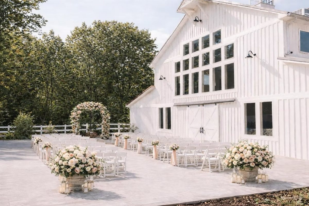 White modern barn wedding venue with outdoor ceremony seating and floral arrangements.