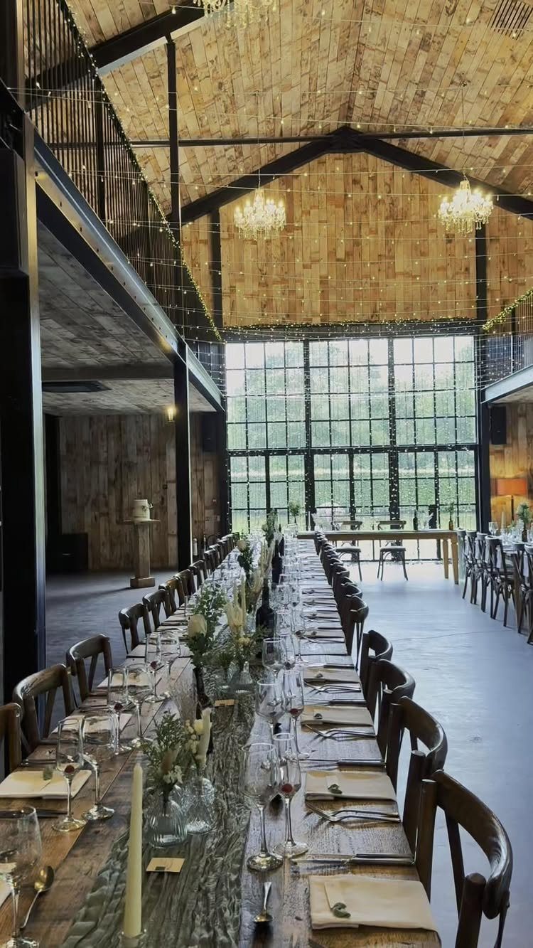Long wooden wedding table in a barn with black steel beams and chandeliers.