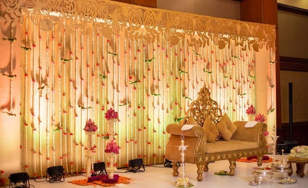 15 Seemantham Decoration Ideas for a Joyful Baby Shower 4 Ornate gold carved wooden sofa with cushions against a floral string backdrop.