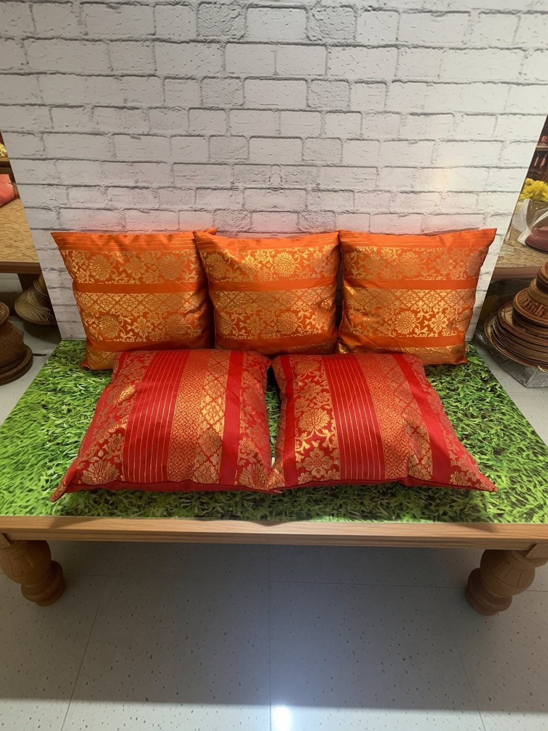 15 Seemantham Decoration Ideas for a Joyful Baby Shower 5 Vibrant orange and red ethnic silk cushions on a green mat and wooden platform.