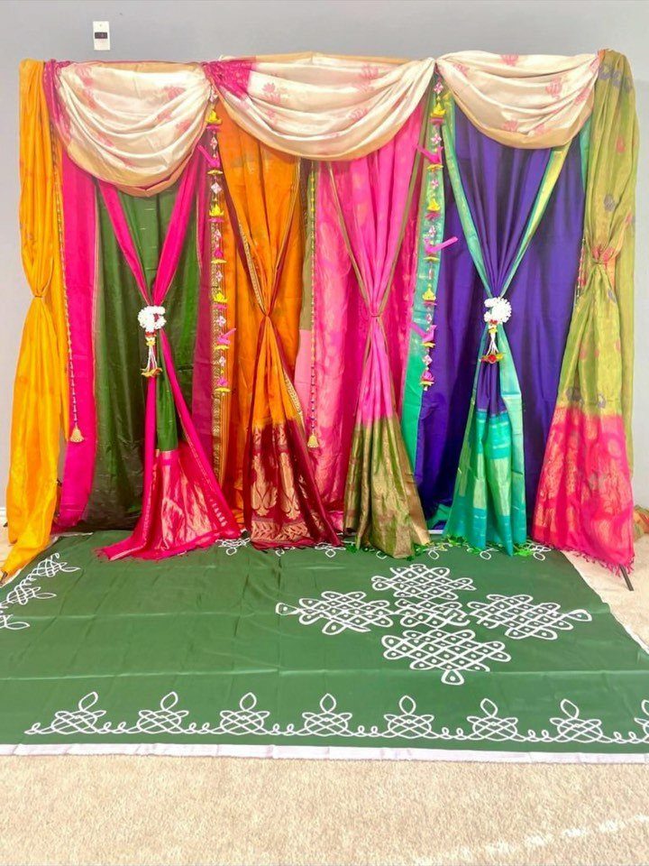 15 Seemantham Decoration Ideas for a Joyful Baby Shower 11 Colorful draped fabric backdrop with a green rangoli mat on the floor.