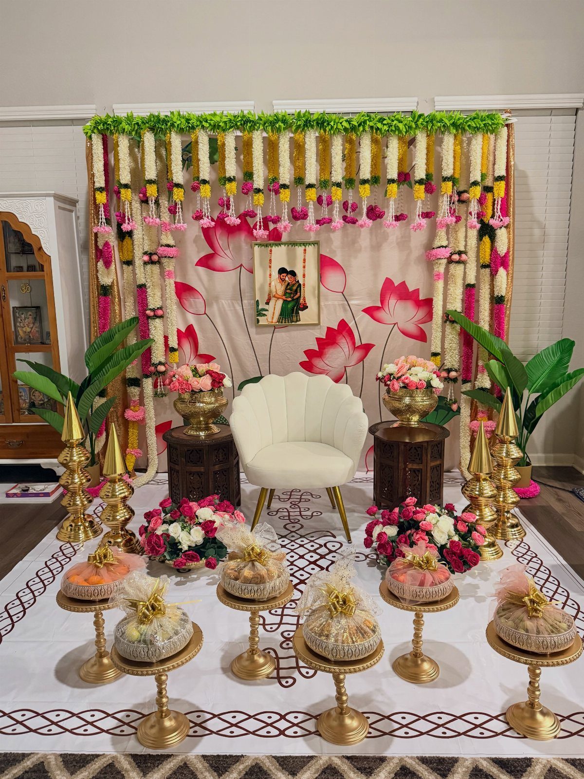 15 Seemantham Decoration Ideas for a Joyful Baby Shower 15 Festive event setup with a white chair, floral backdrop, and gold brass lamps.