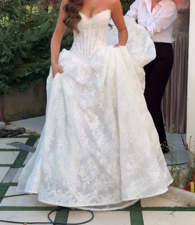 White lace wedding dress with a sweetheart neckline worn by a woman outdoors.