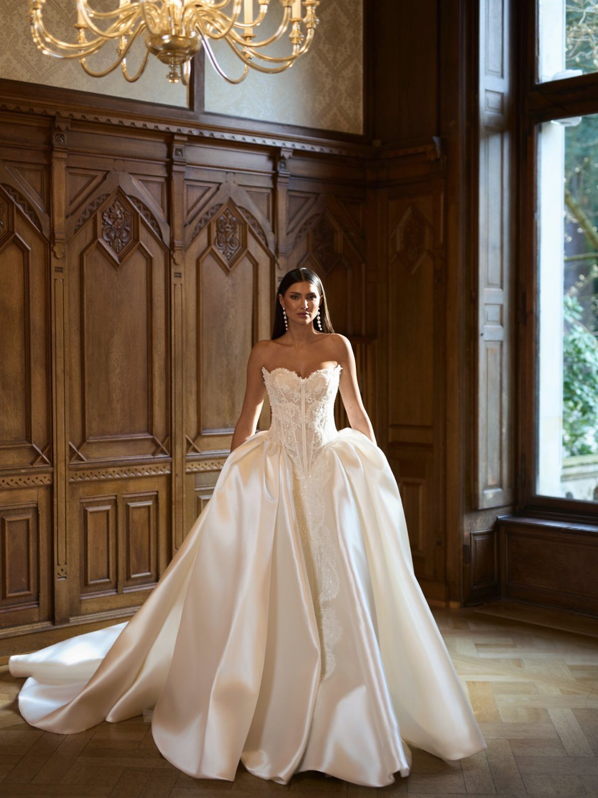 Woman in a white satin sweetheart wedding dress standing in a wood-paneled room.