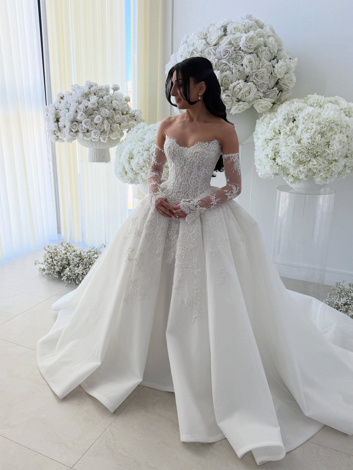 Woman in a white sweetheart neckline wedding dress surrounded by white rose bouquets