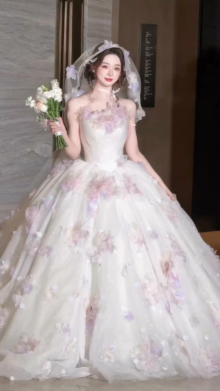 Woman in a white floral sweetheart wedding dress with a veil and bouquet.
