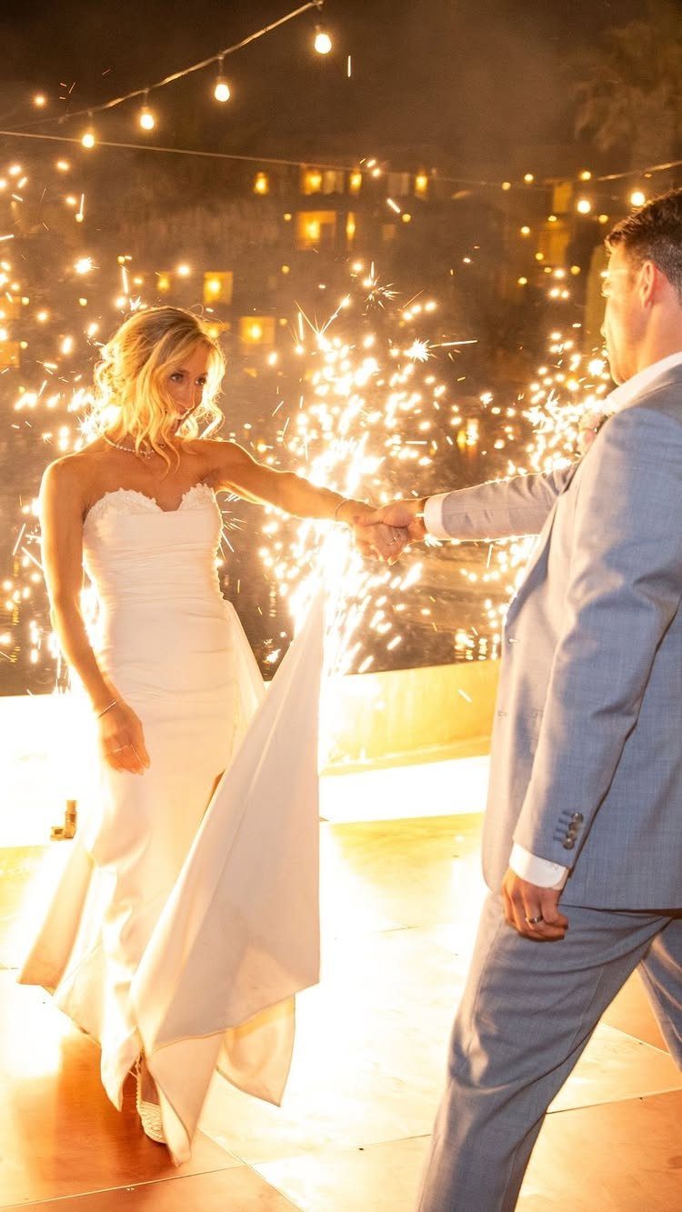 Bride in sweetheart wedding dress with train dancing with groom amidst bright sparklers.