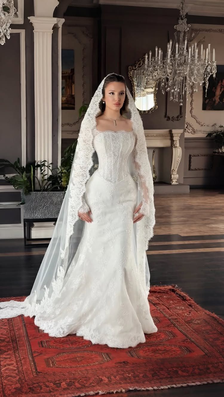 Woman in a white lace sweetheart wedding dress and long veil standing indoors.