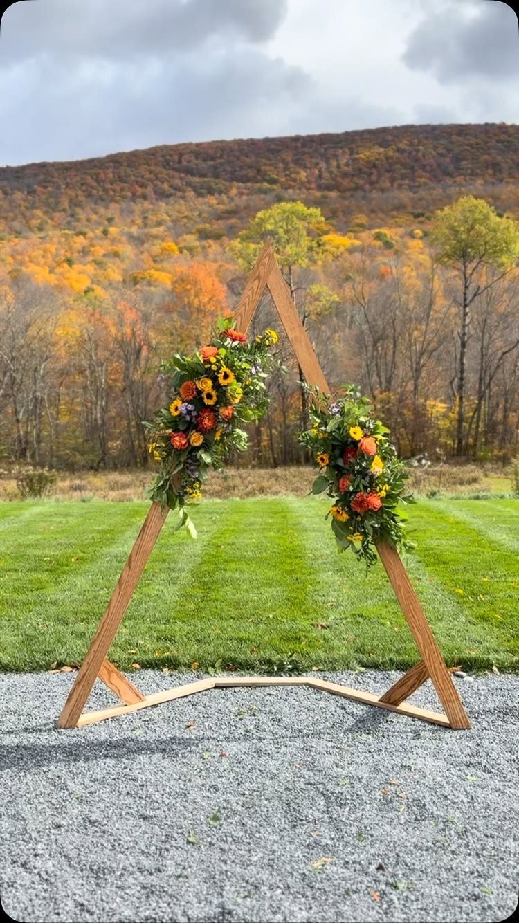 Wooden triangle wedding arch decorated with autumn flowers and greenery against fall mountains.