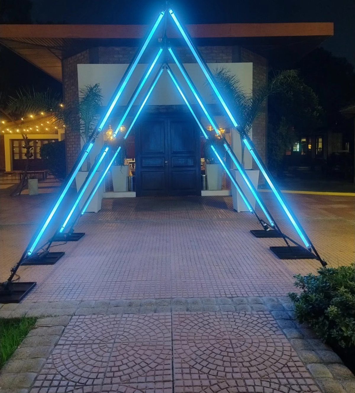 Triangular arch with bright blue neon lights on a brick patio at night