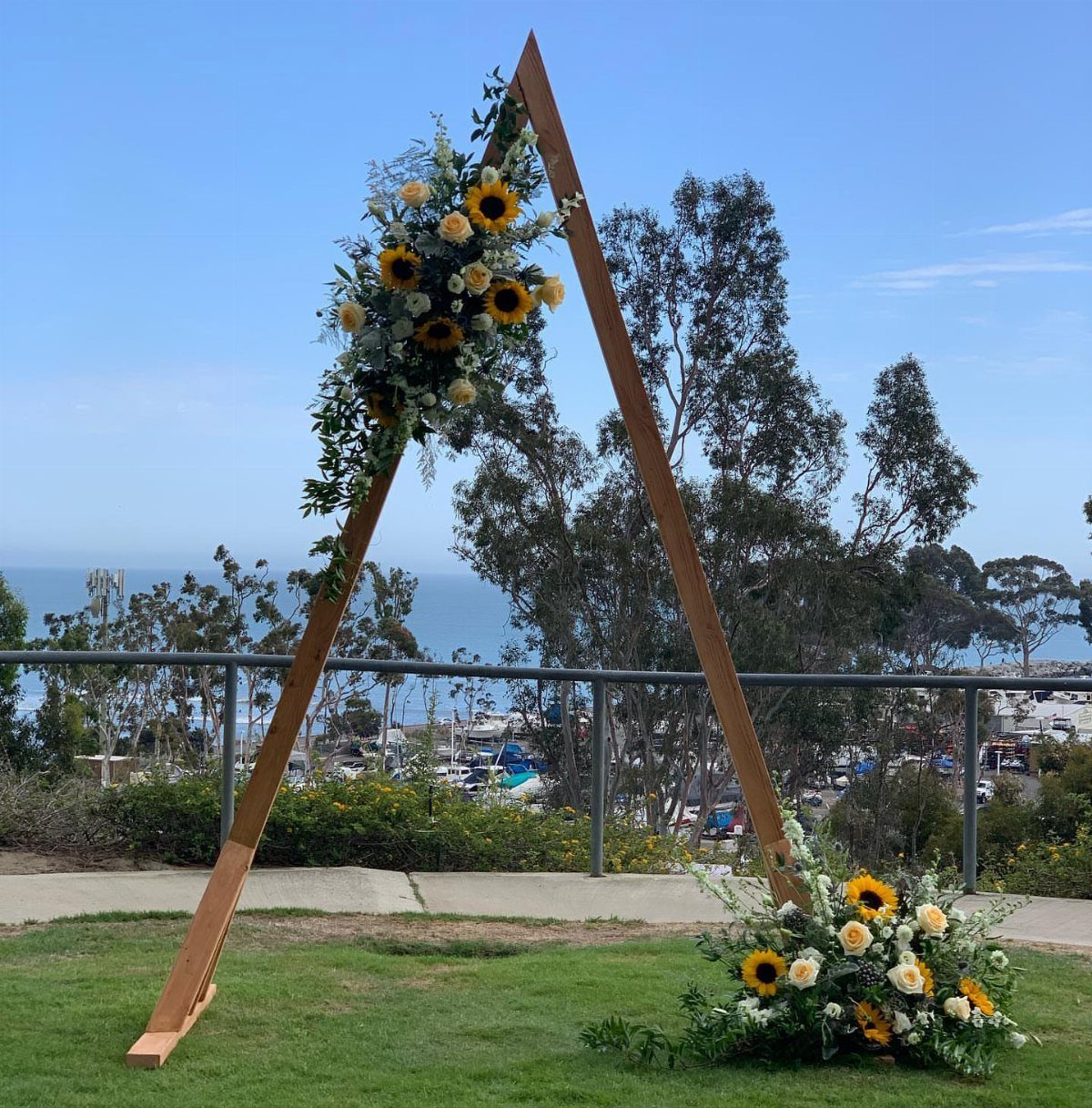 Wooden triangle wedding arch decorated with sunflowers and white flowers outdoors by the ocean