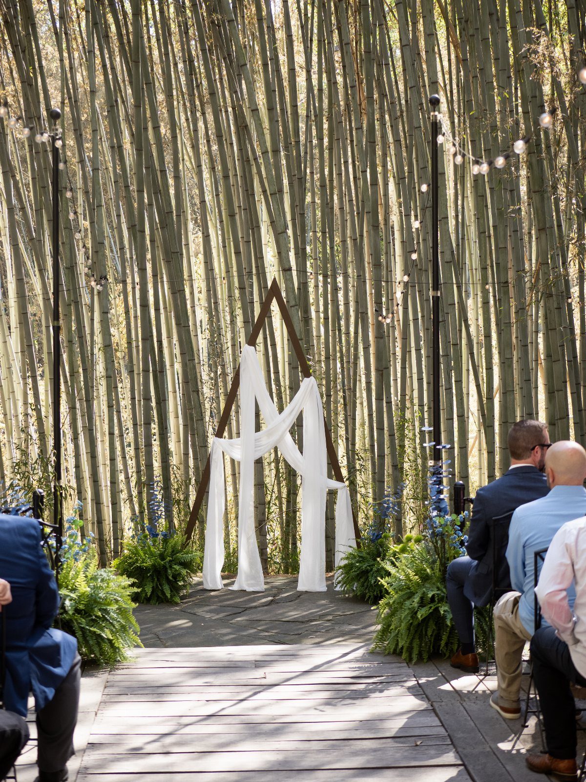 Wooden triangle wedding arch with white fabric draping in a bamboo forest setting