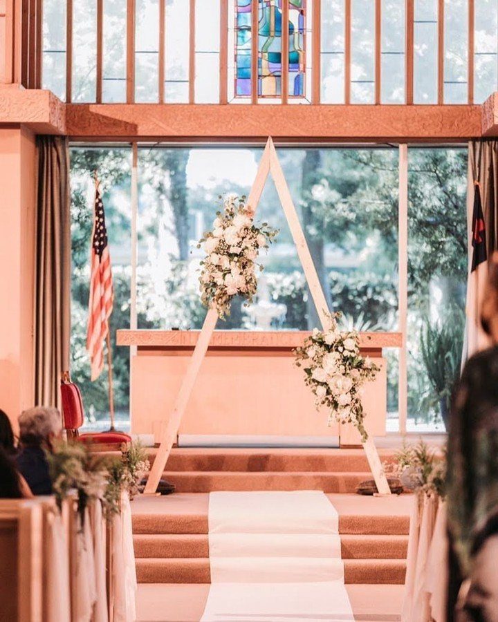 Wooden triangle wedding arch with white floral arrangements in a bright chapel