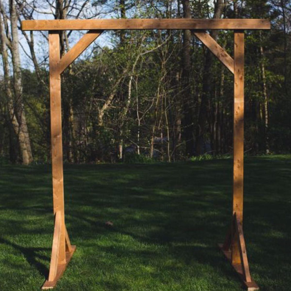 Wooden wedding arch with flat base plates standing on a green grassy lawn