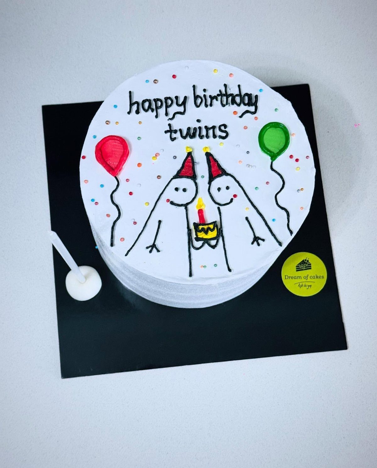 White birthday cake with stick figure drawings and balloons for twins birthday celebration