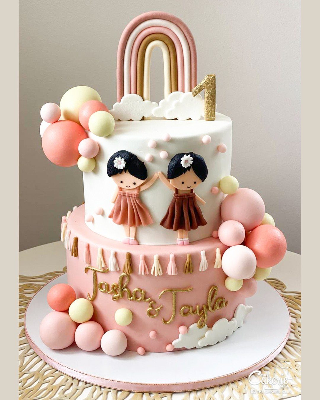 Two-tiered pink and white birthday cake with cartoon girls and a rainbow topper.