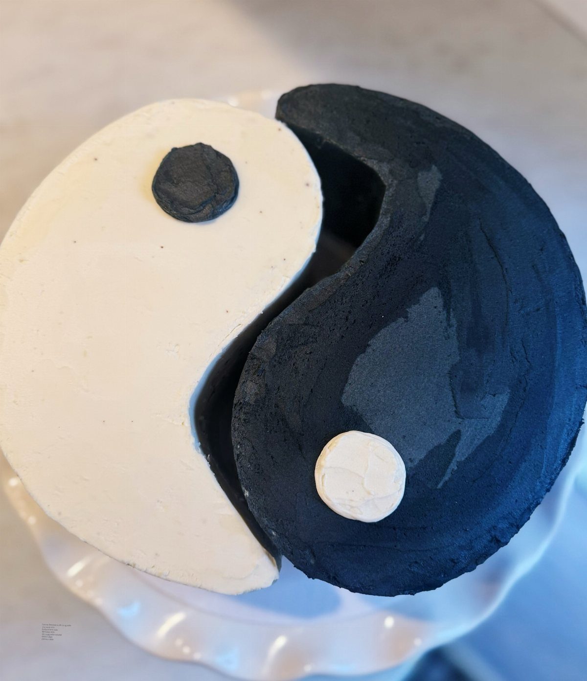 Yin yang cake with contrasting black and white frosting on a white stand.