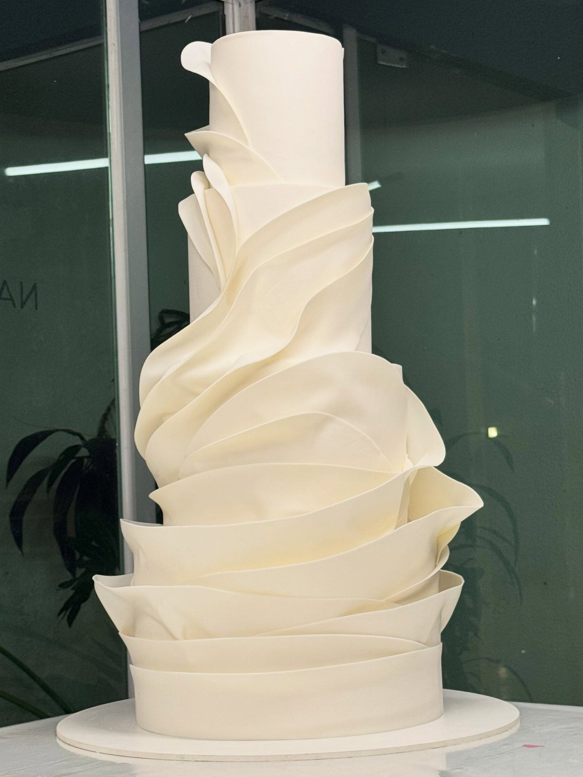 Tall white wedding cake with large, curved asymmetrical fondant ruffles swirling around tiers.