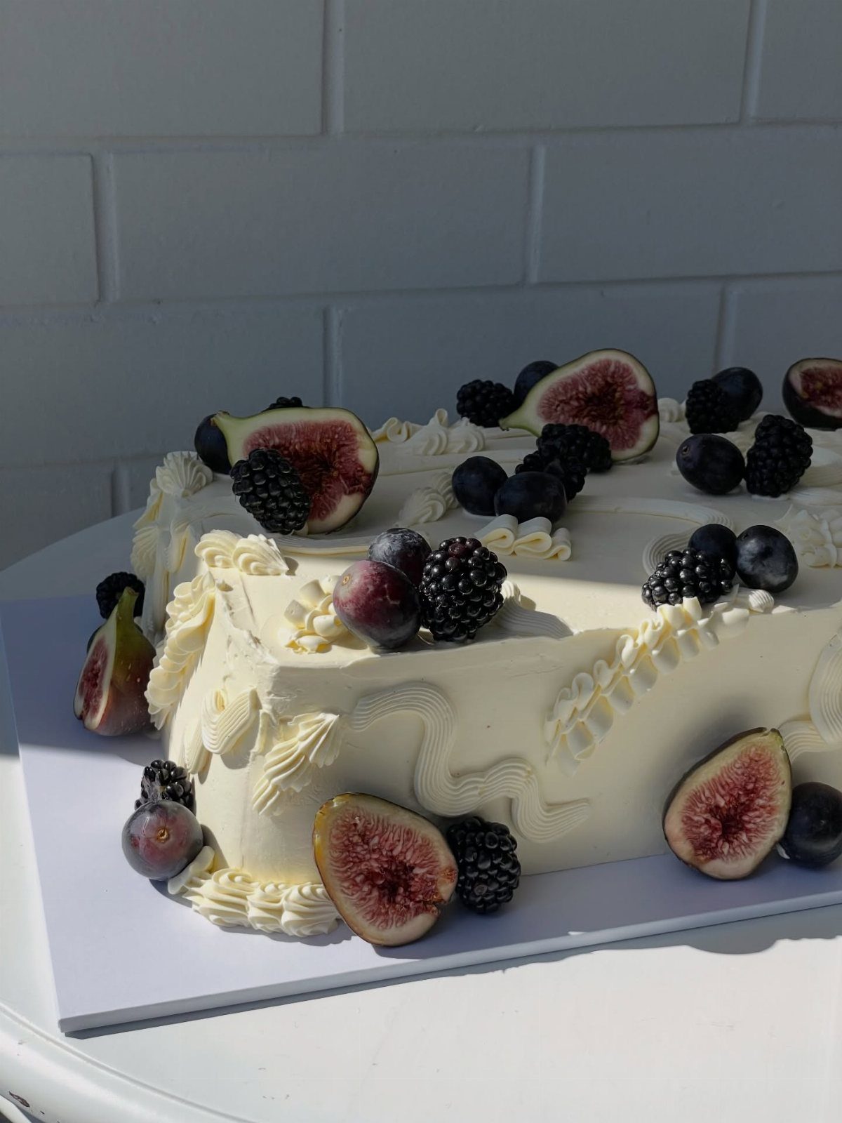 White buttercream cake decorated with fresh sliced figs, blackberries, and blueberries.