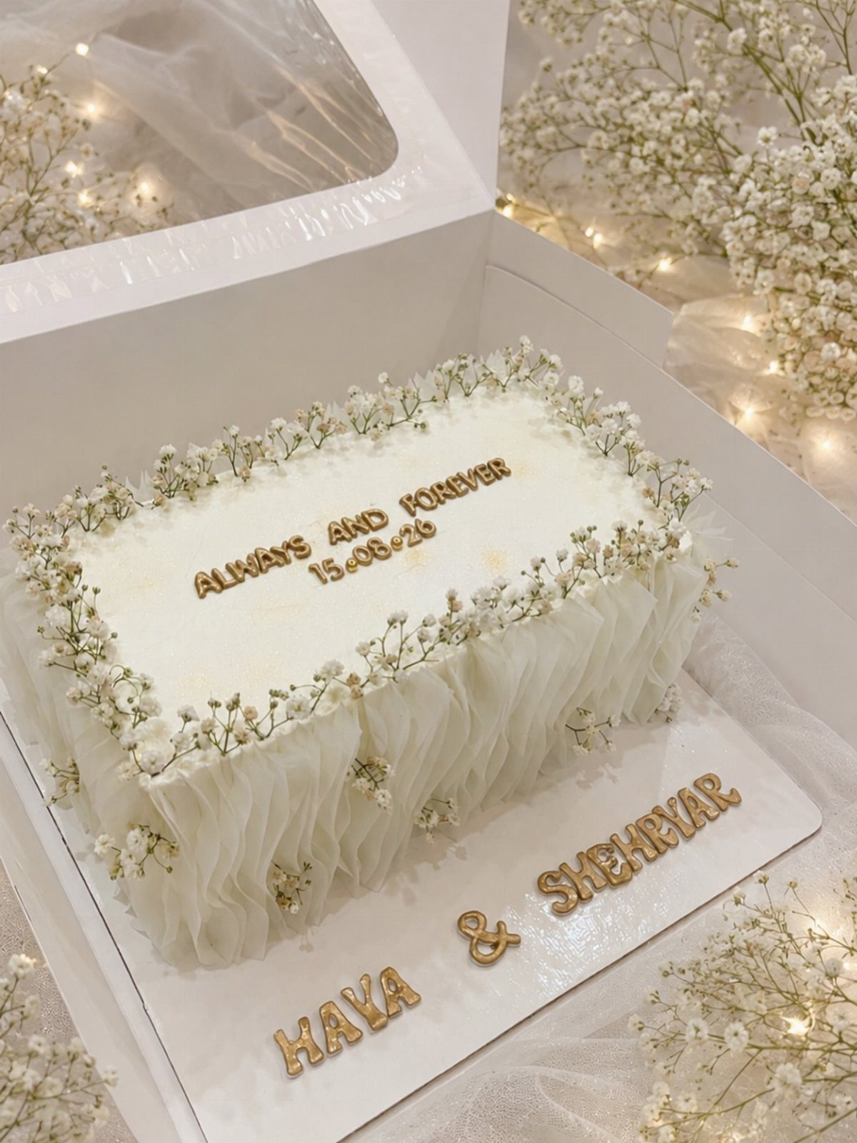 Rectangular white wedding cake decorated with baby's breath flowers and gold lettering.
