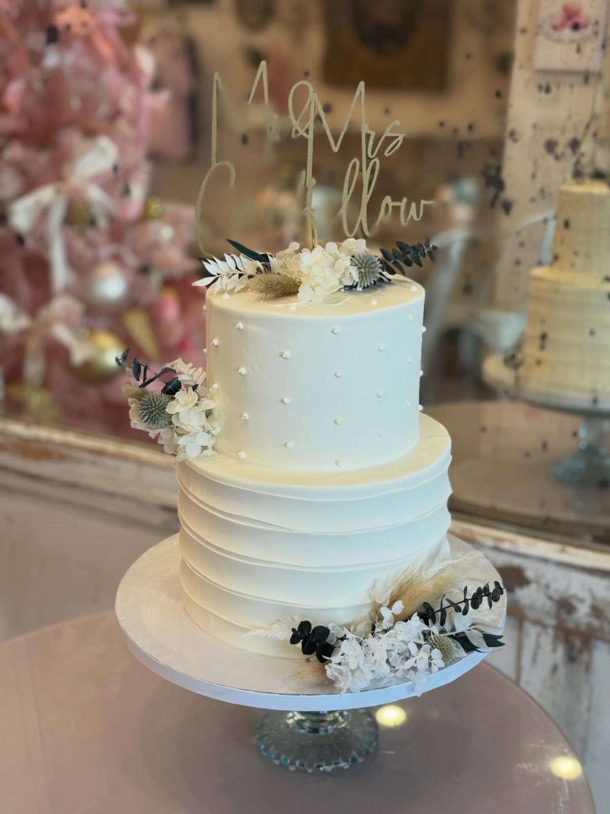 Two-tier white wedding cake with ribbed frosting, white flowers, and gold topper.