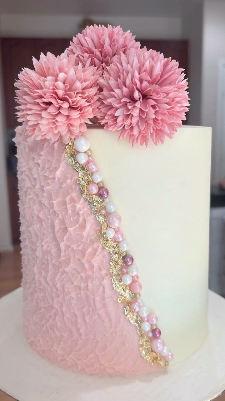 Single-tier cake with white and textured pink buttercream, topped with pink sugar flowers.