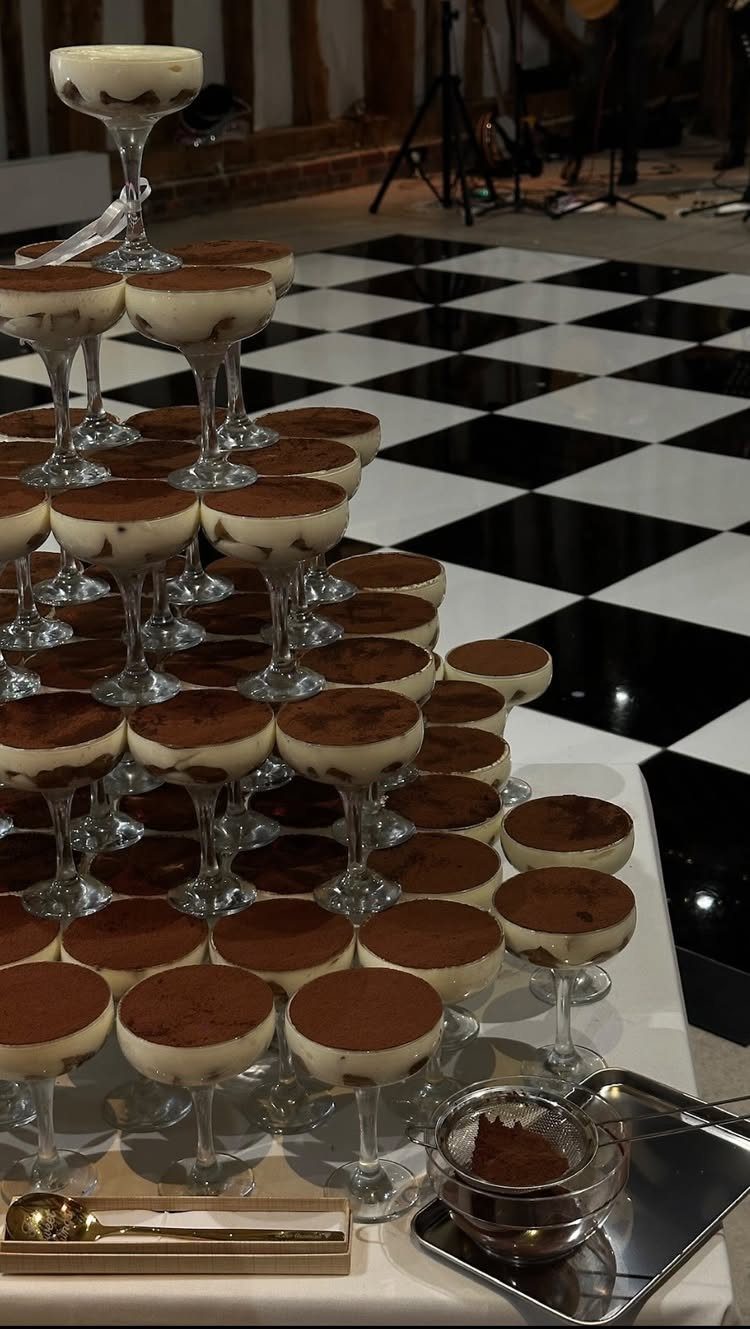 Tiramisu dessert tower in glass coupes on a white table with checkered flooring.