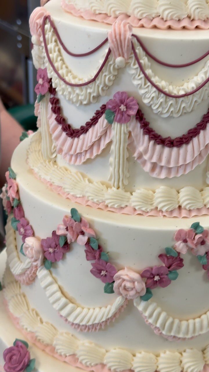 Multi-tiered white cake with ornate vintage Lambeth piping and small pink frosting flowers.