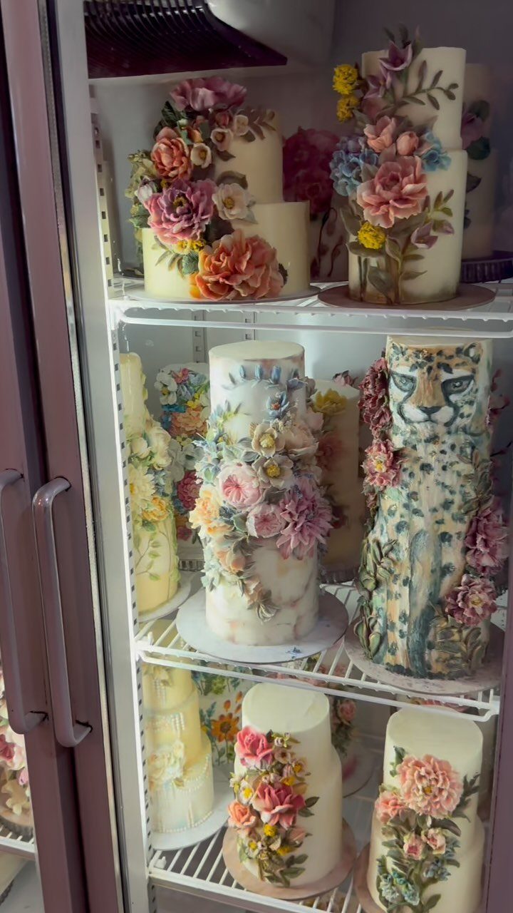 Tiered white cakes decorated with colorful floral frosting inside a refrigerator.