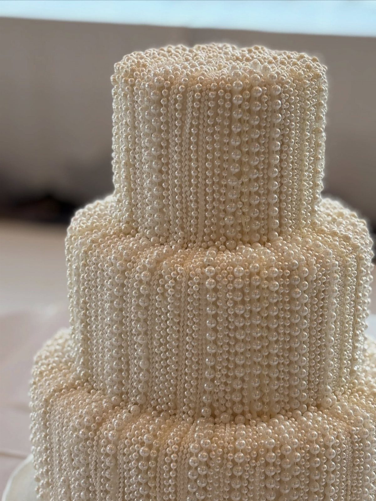 Three-tiered white wedding cake entirely covered in small, shimmering white edible pearls.