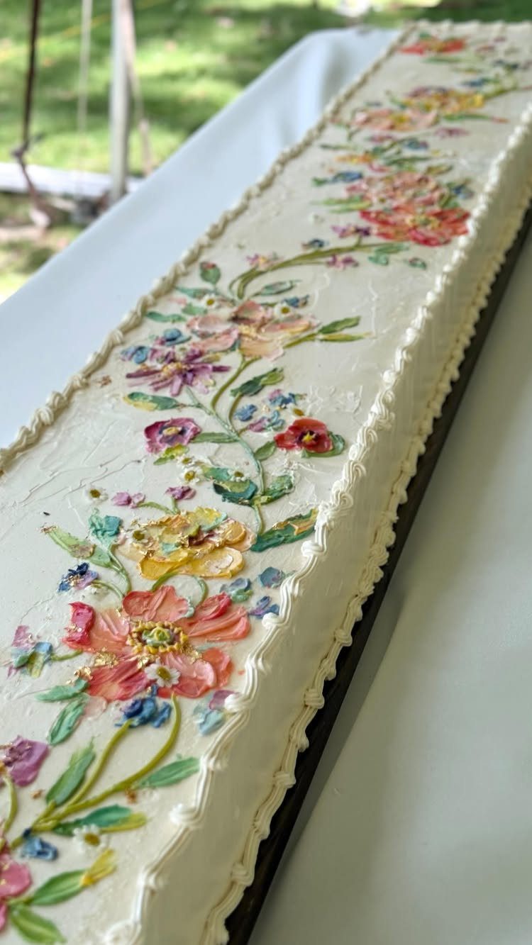 Rectangular white sheet cake decorated with colorful buttercream flowers and a scalloped border.