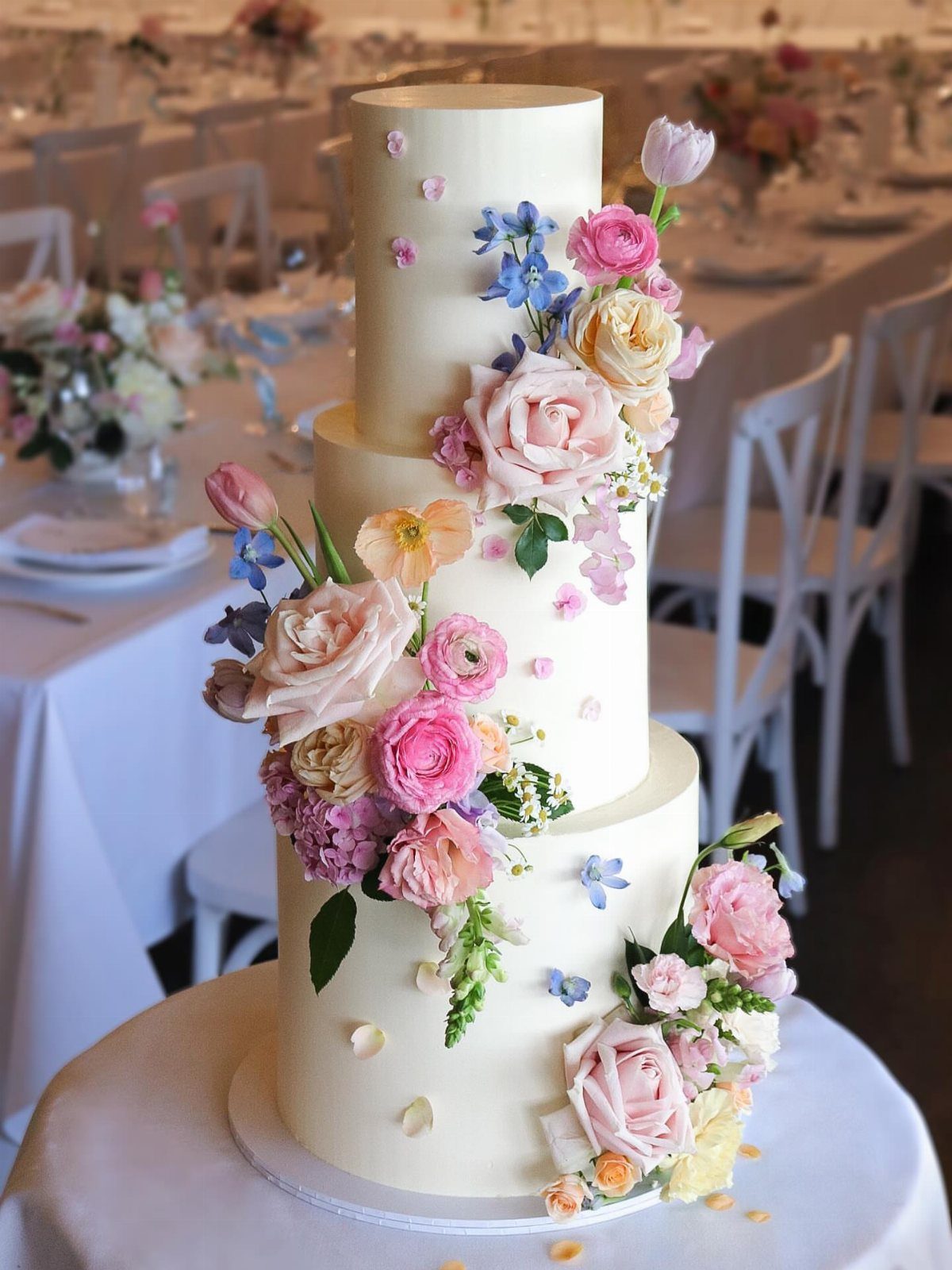 37 Wedding Cakes with Flowers to Inspire Your Design 16 Three-tier white wedding cake adorned with vibrant pink, blue, and peach fresh flowers.