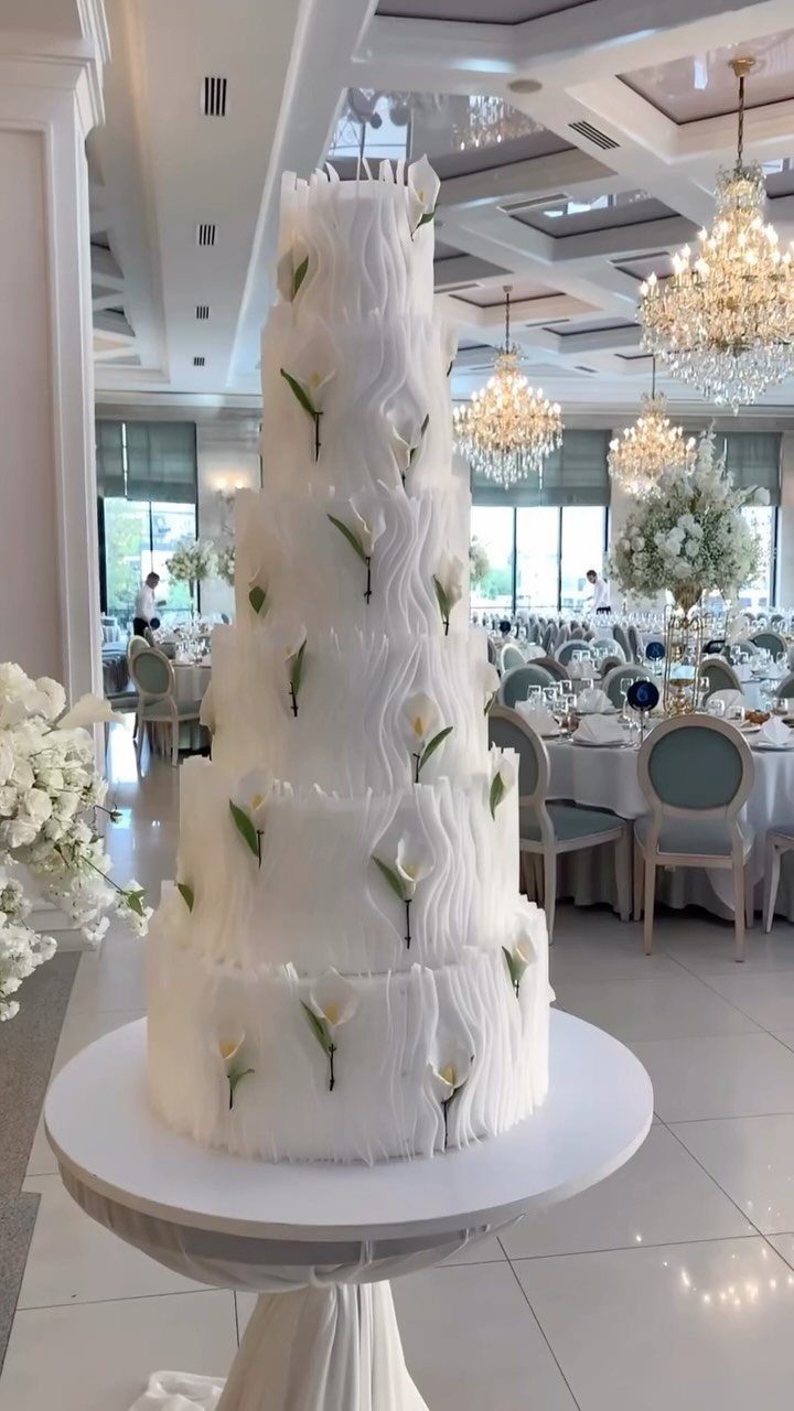 37 Wedding Cakes with Flowers to Inspire Your Design 37 Tall white tiered wedding cake decorated with calla lilies in a bright ballroom.