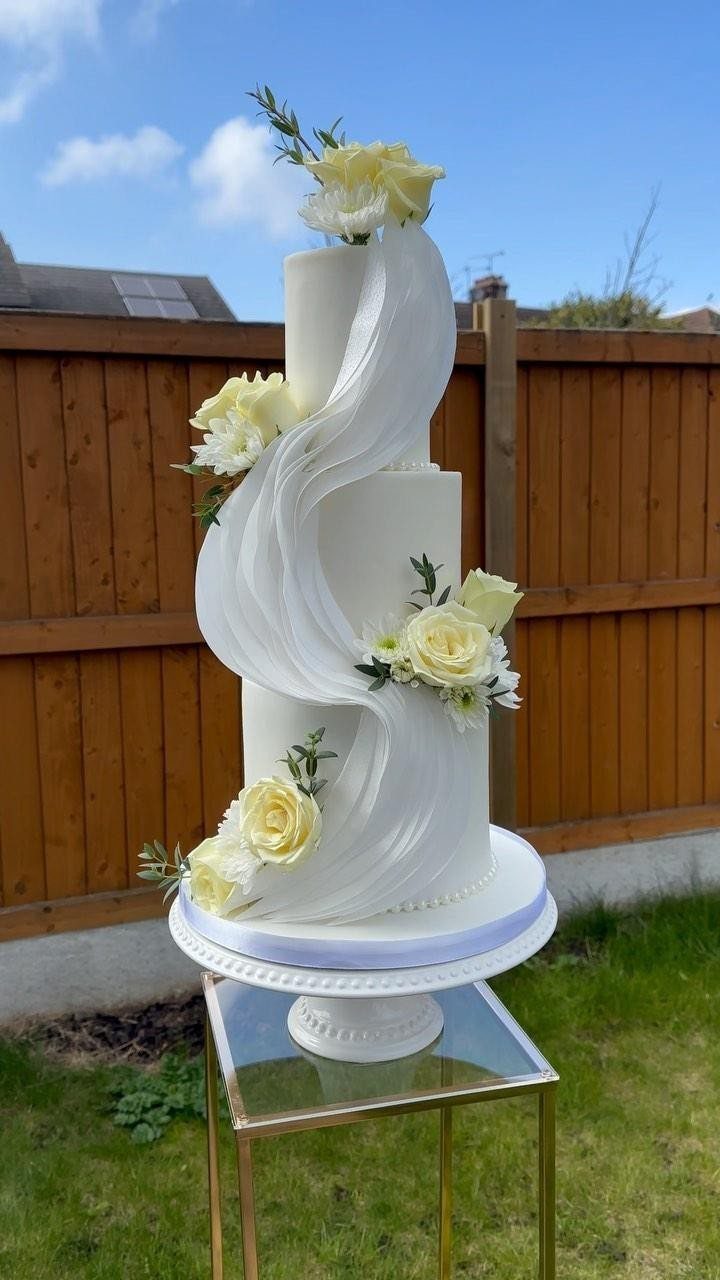 37 Wedding Cakes with Flowers to Inspire Your Design 2 Three-tier white wedding cake with a cascading fondant swirl and pale yellow roses.