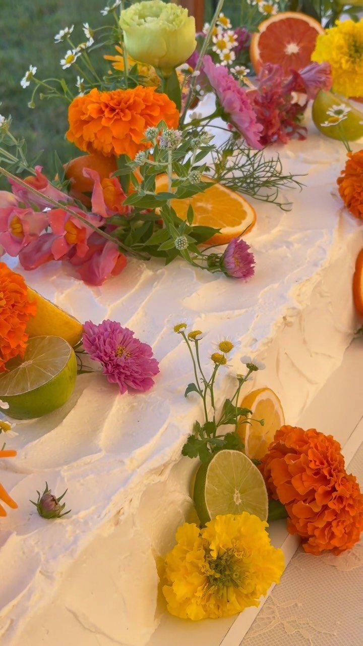 37 Wedding Cakes with Flowers to Inspire Your Design 8 White frosted cake decorated with citrus slices, colorful marigolds, and fresh greenery.