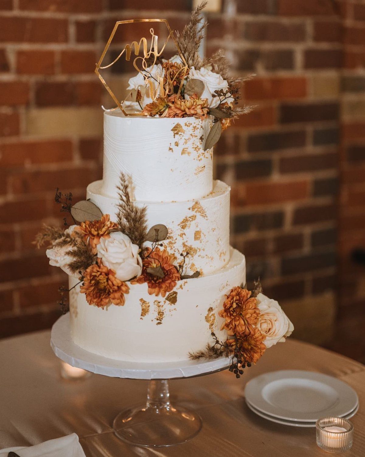 37 Wedding Cakes with Flowers to Inspire Your Design 18 Three-tier white wedding cake with gold leaf and earthy orange and cream flowers.