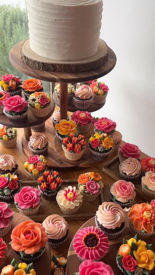 37 Wedding Cakes with Flowers to Inspire Your Design 23 Floral cupcakes in vibrant colors arranged around a white tiered wedding cake.