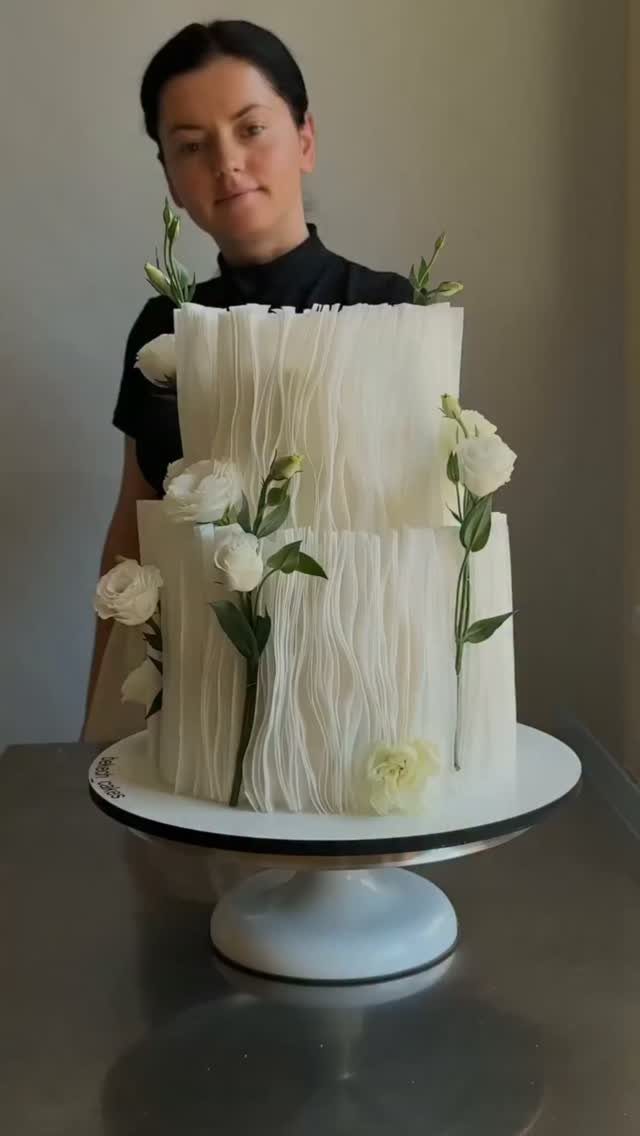 37 Wedding Cakes with Flowers to Inspire Your Design 11 Two-tier white textured cake decorated with long-stemmed white roses on a white stand.