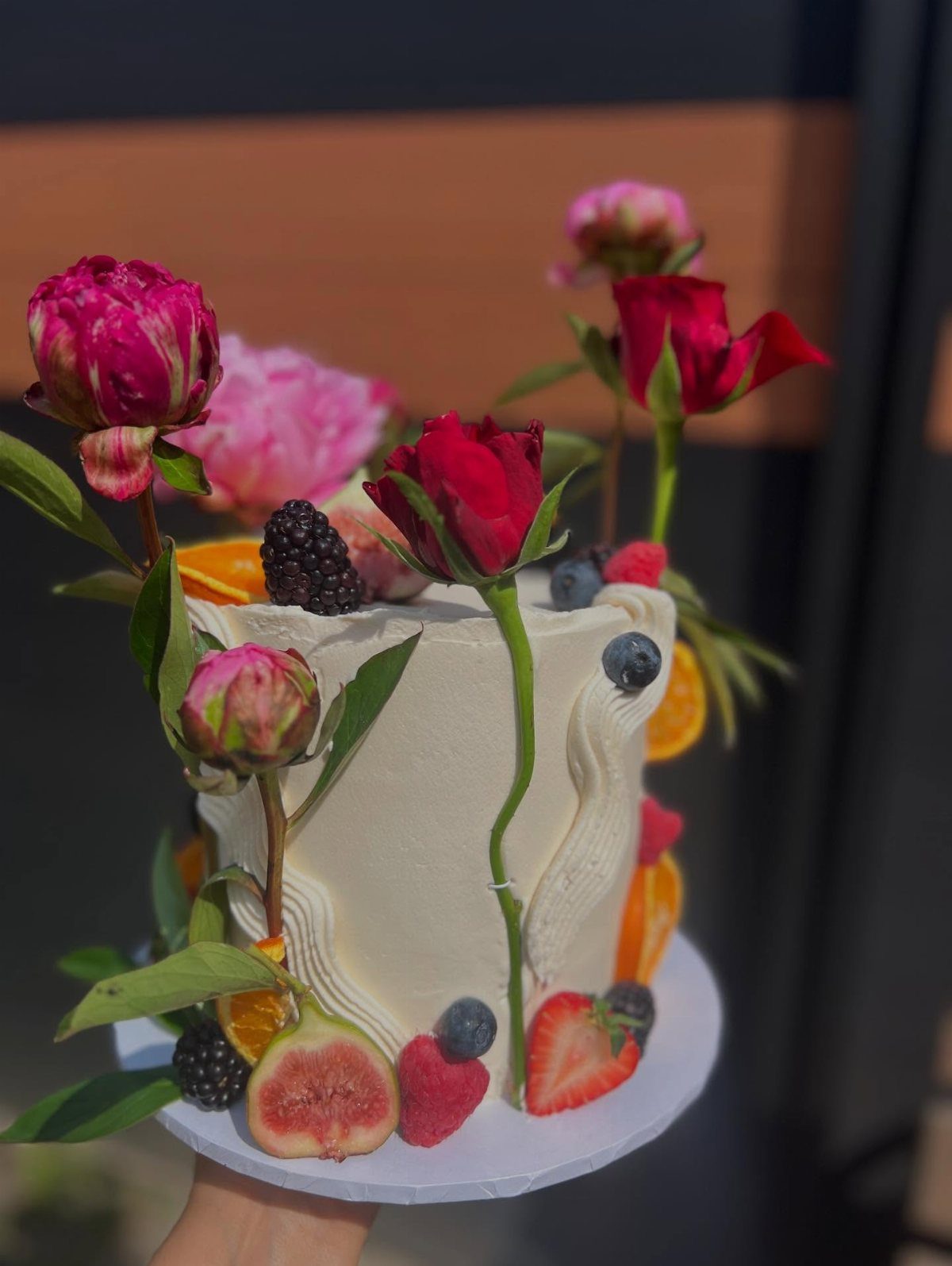 37 Wedding Cakes with Flowers to Inspire Your Design 26 White frosted cake decorated with fresh red roses, berries, orange slices, and figs.