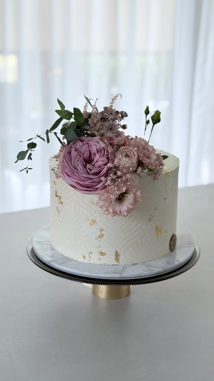 37 Wedding Cakes with Flowers to Inspire Your Design 21 White textured cake with purple roses and gold leaf accents on a marble stand