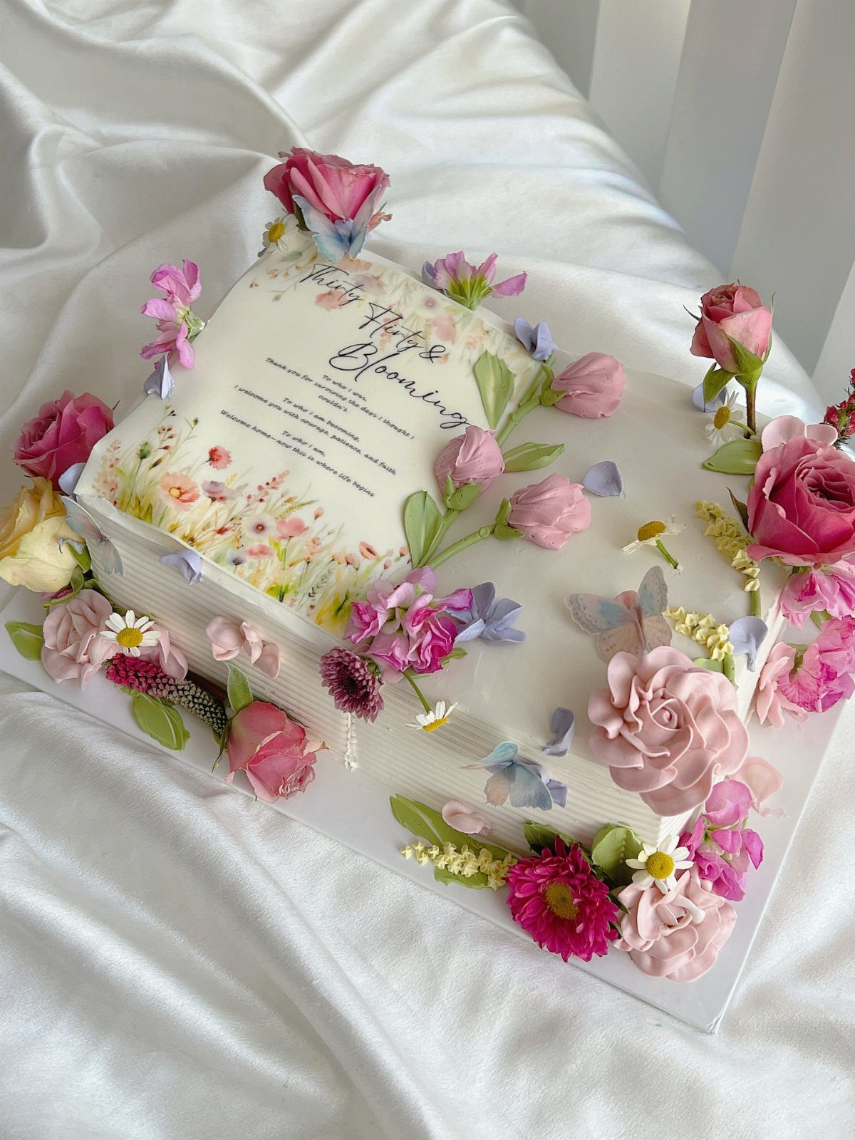 37 Wedding Cakes with Flowers to Inspire Your Design 15 Book shaped cake with painted floral pages and fresh pink and purple flowers.
