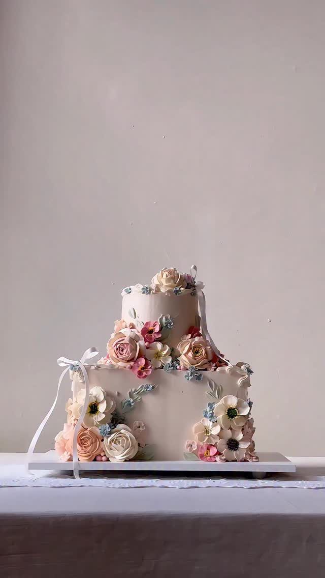 37 Wedding Cakes with Flowers to Inspire Your Design 31 Two-tier white cake decorated with pastel pink, peach, and blue sugar flowers.