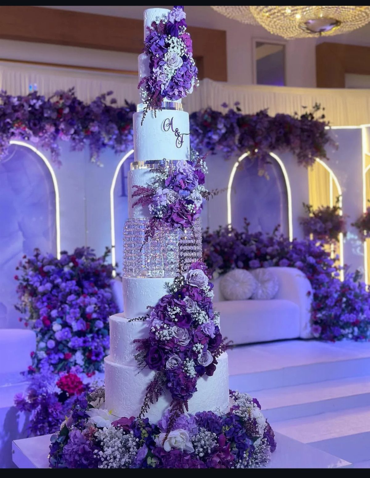 37 Wedding Cakes with Flowers to Inspire Your Design 9 Tall white wedding cake with cascading deep purple and lavender floral arrangements.
