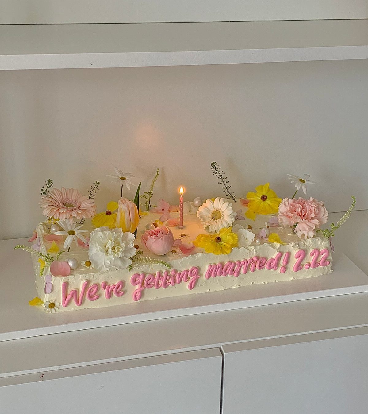 37 Wedding Cakes with Flowers to Inspire Your Design 4 White rectangular cake with scattered pink and yellow flowers and a lit candle.