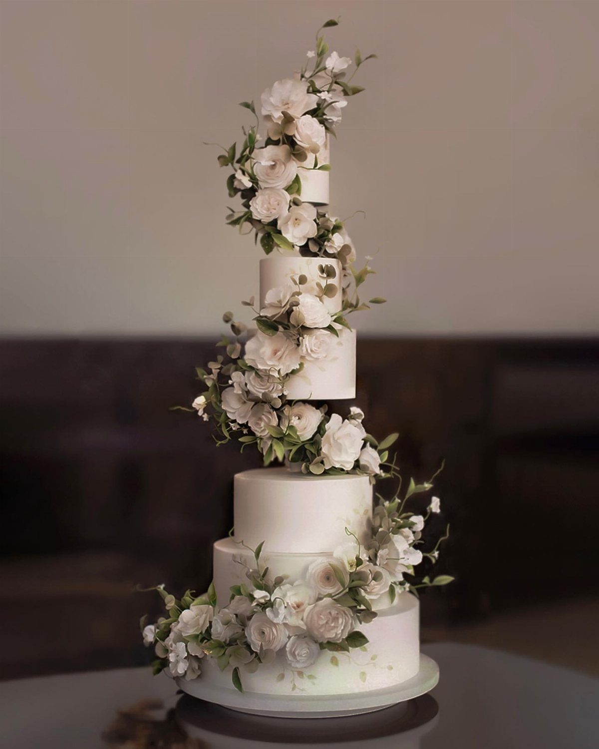 37 Wedding Cakes with Flowers to Inspire Your Design 20 White multi-tiered wedding cake with white roses and greenery sweeping up the sides.