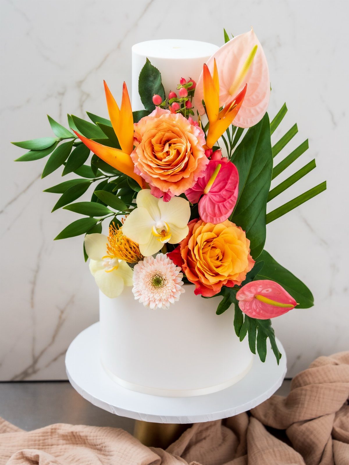 37 Wedding Cakes with Flowers to Inspire Your Design 36 White two-tier wedding cake adorned with colorful tropical flowers and lush green leaves.